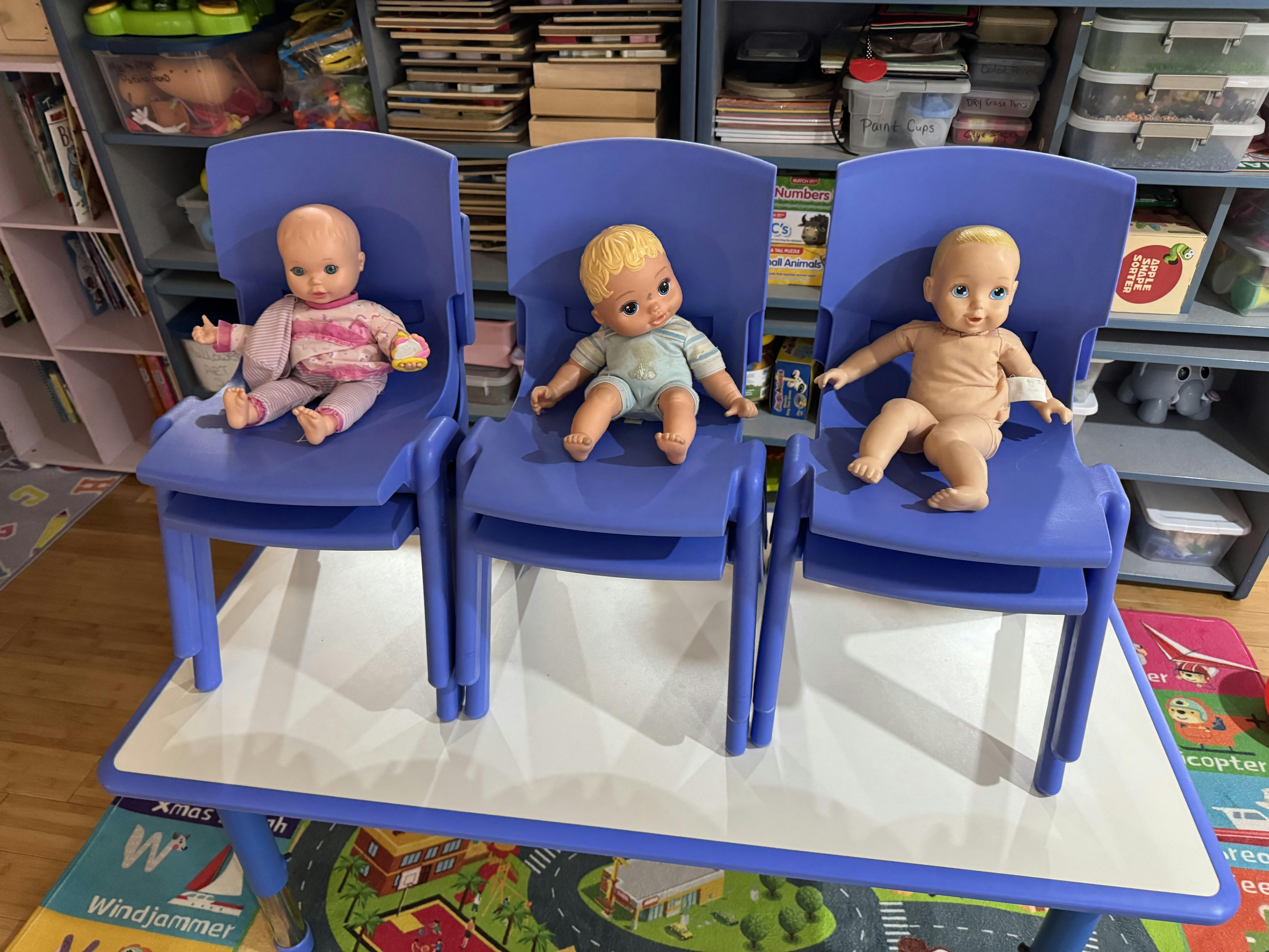 Three baby dolls sitting on small blue plastic chairs