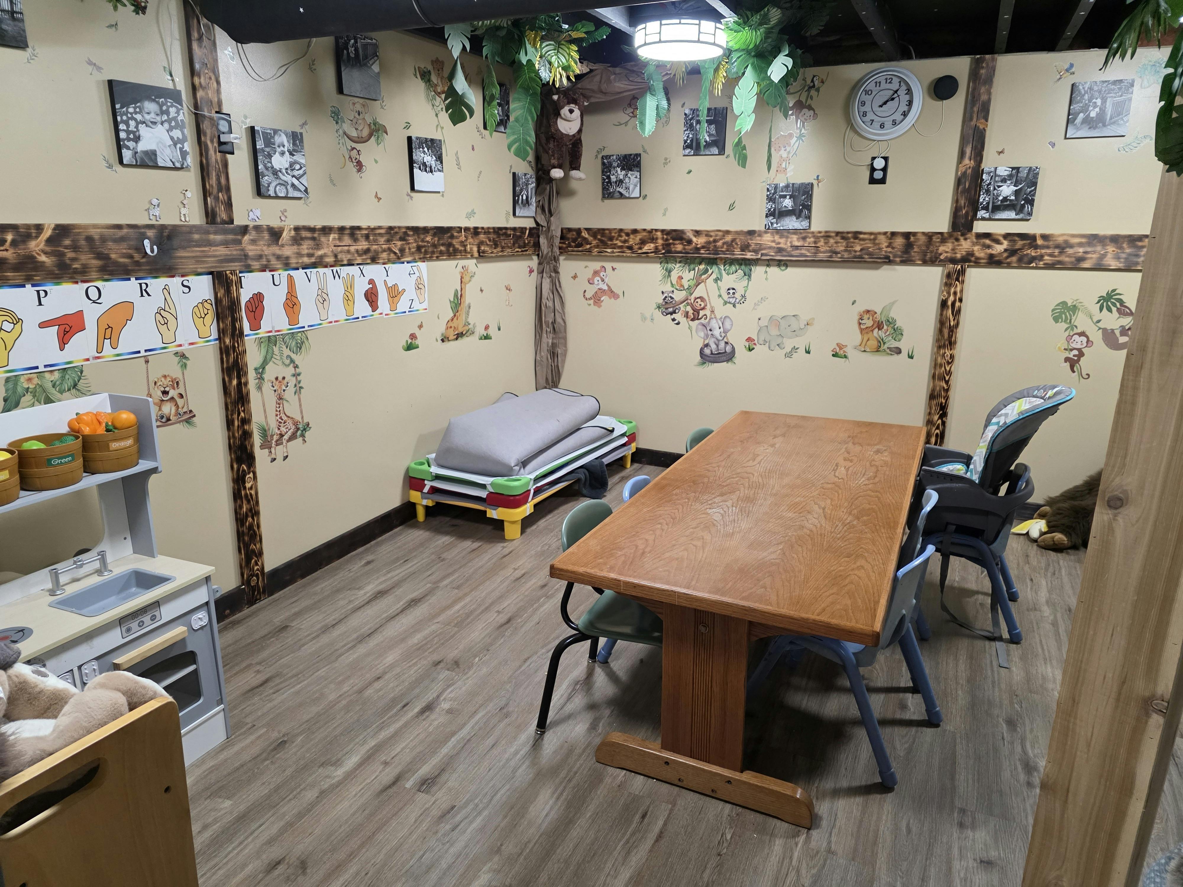 Childcare room with a wooden table, chairs, play kitchen, and jungle decor