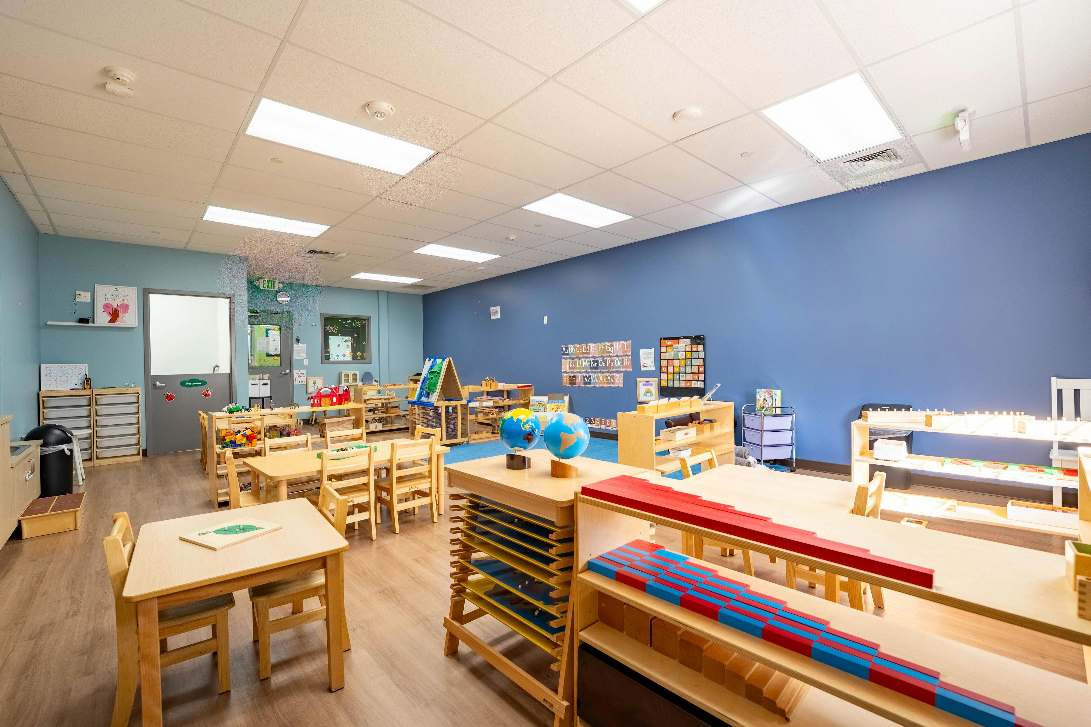 An empty classroom with small wooden tables and chairs, and educational materials