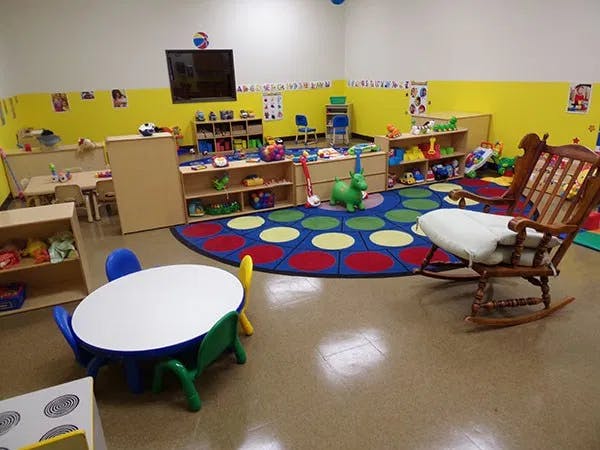 Playroom with a colorful rug, small tables and chairs, and shelves of toys