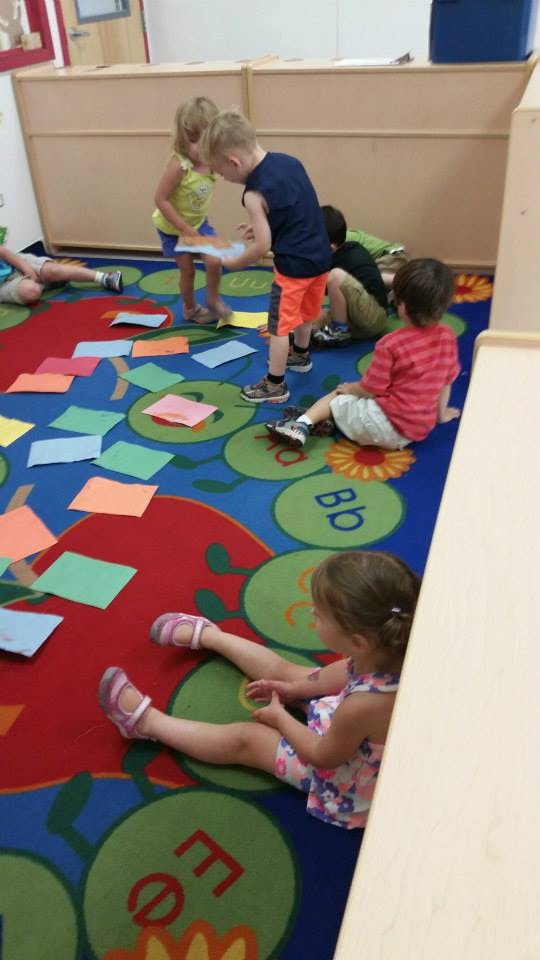 Children playing on a colorful rug with paper squares
