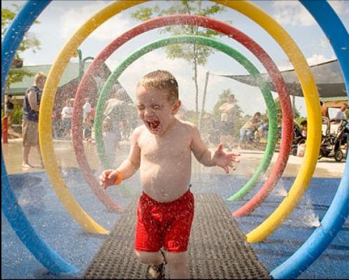 Child in red shorts running through water sprinklers