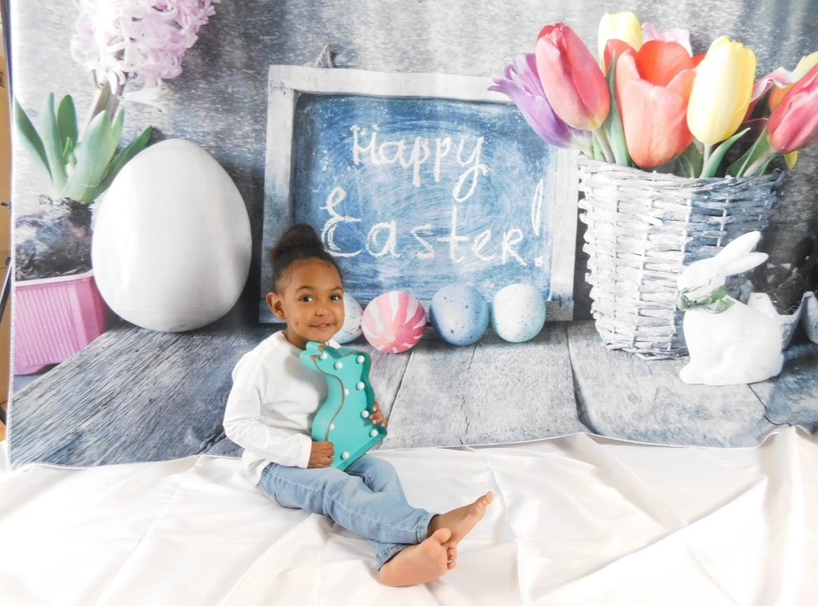 Child sitting with a blue bunny decoration in front of a Happy Easter sign