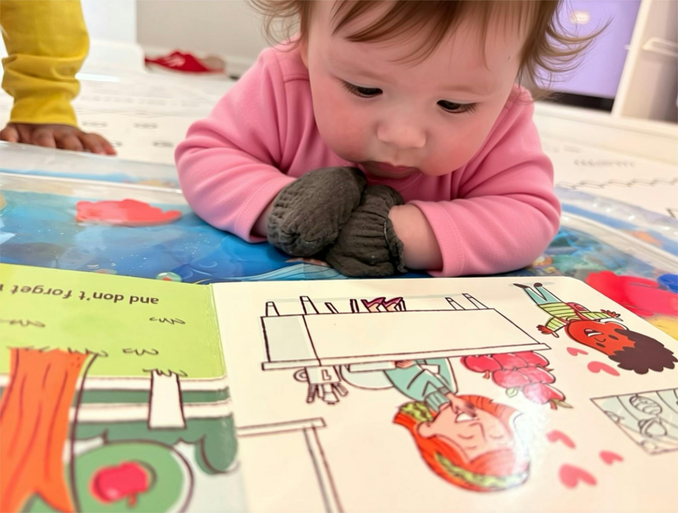Child in a pink shirt playing with a water mat and looking at a book