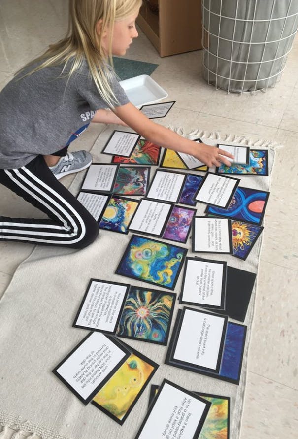 Child kneeling on a rug, arranging cards with text and abstract art