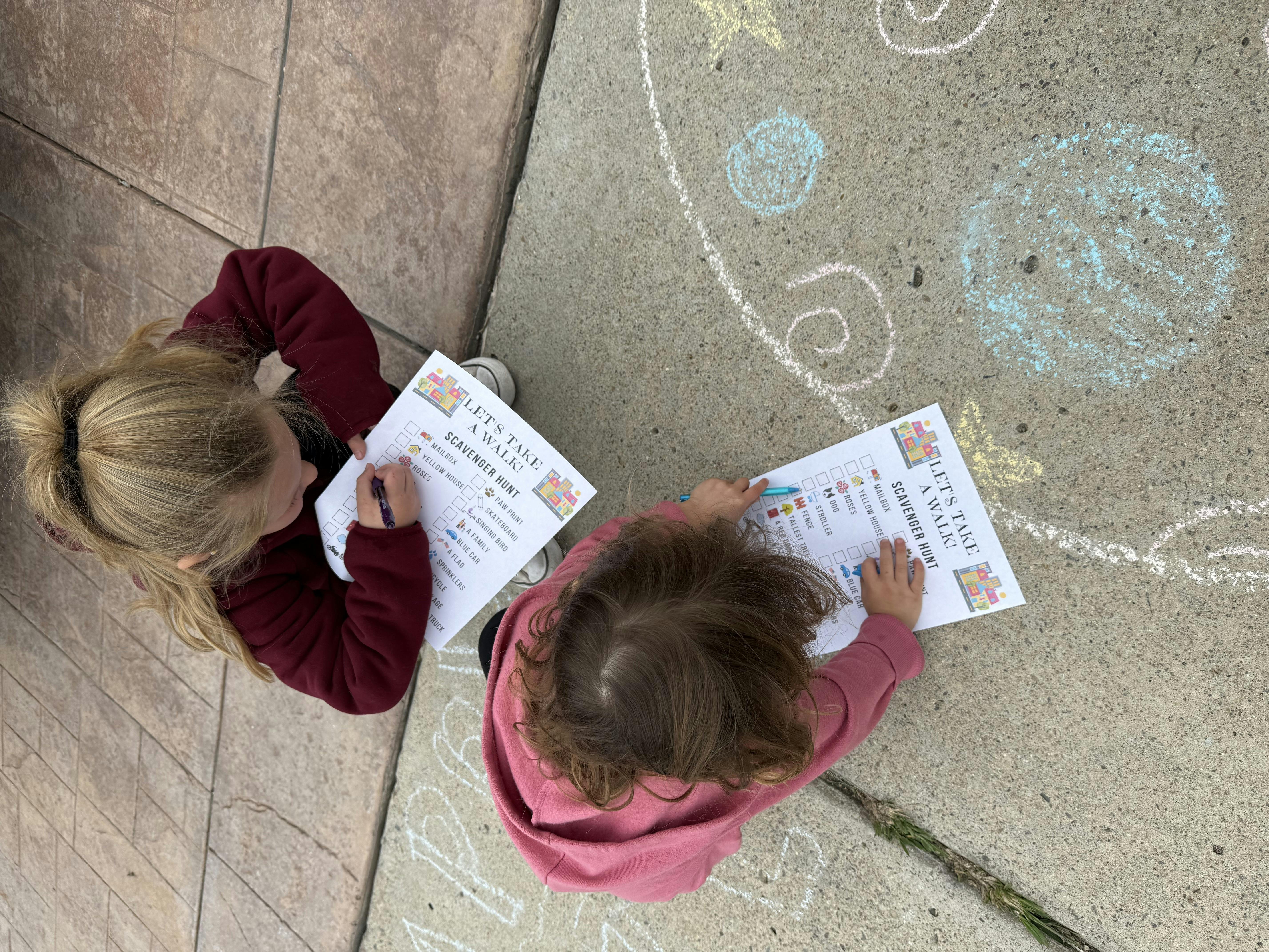Two children writing on papers on the ground with chalk drawings