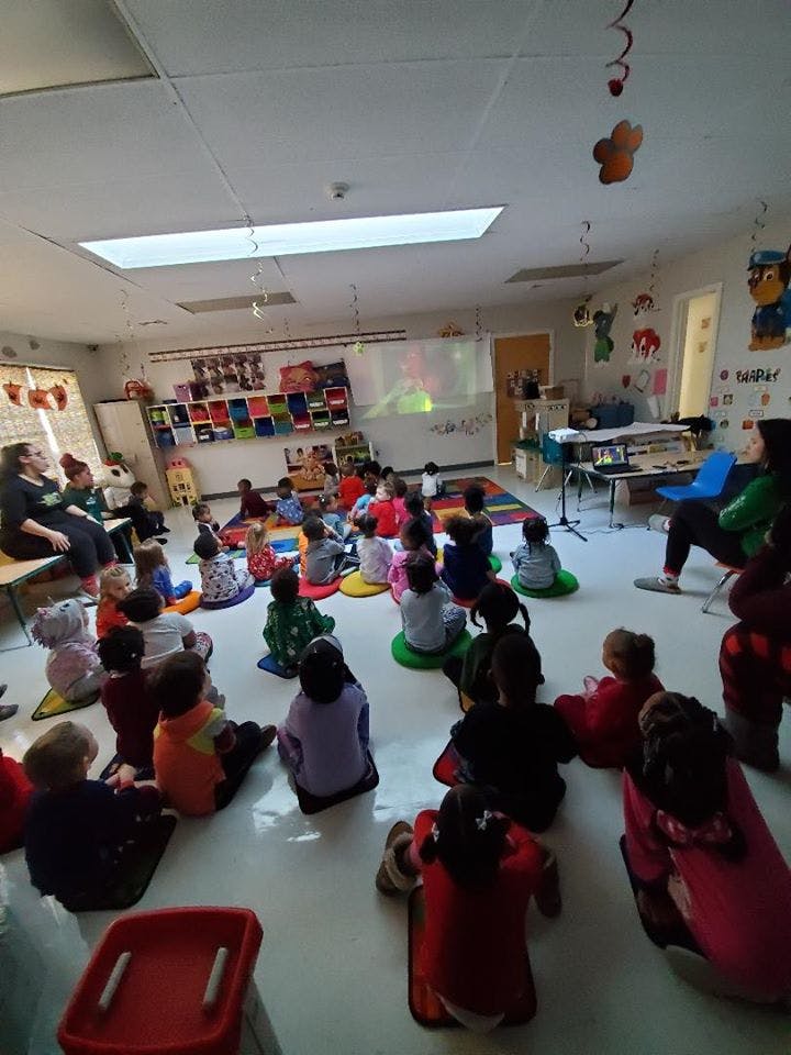 Children sitting on the floor in a classroom, facing a screen