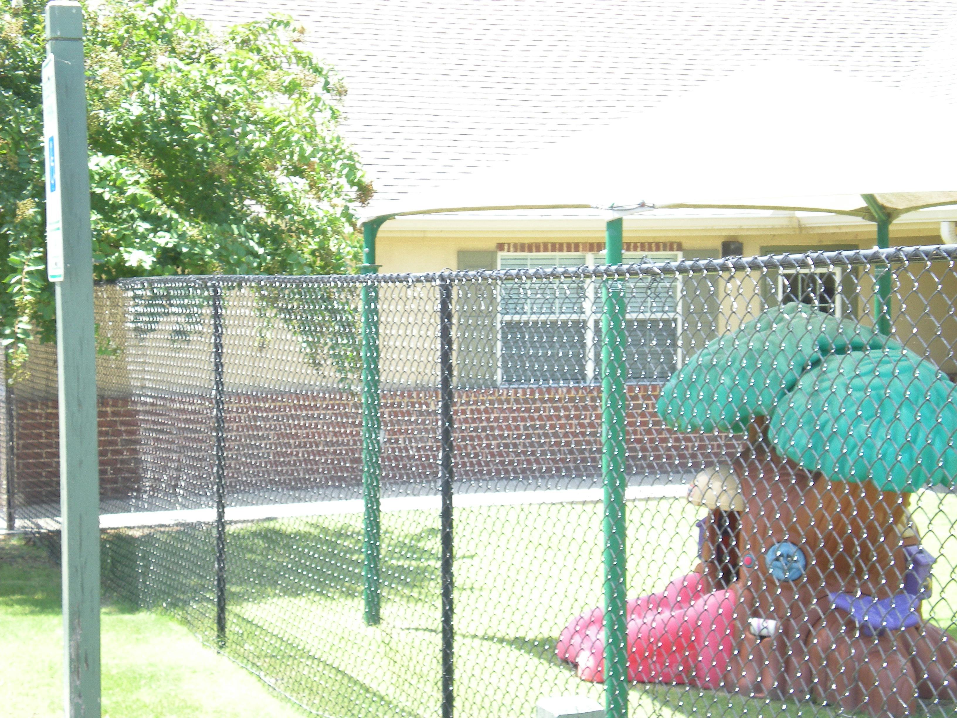 Playground with a tree-shaped play structure and slide behind a fence