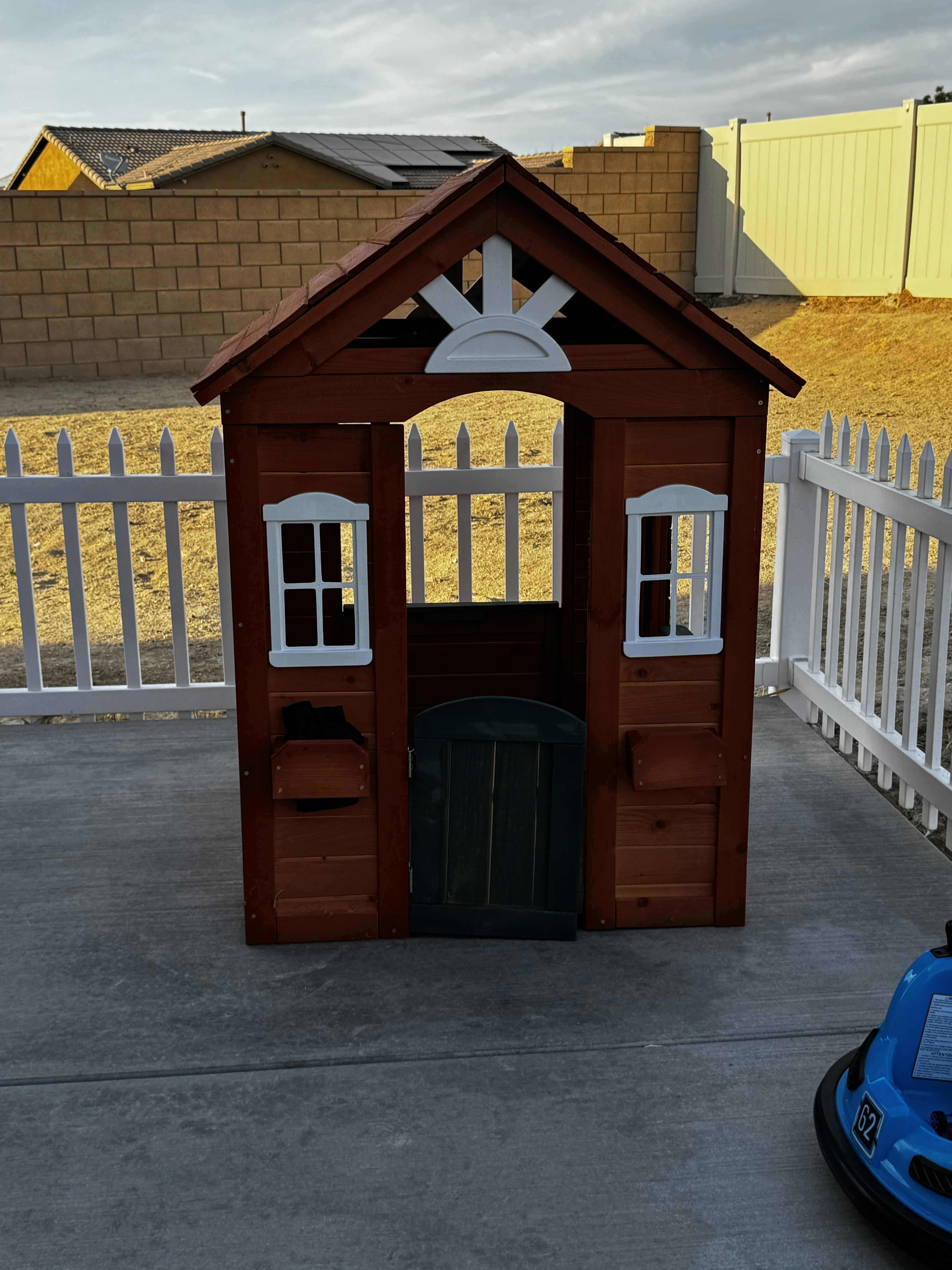 Wooden playhouse on a patio with a white picket fence