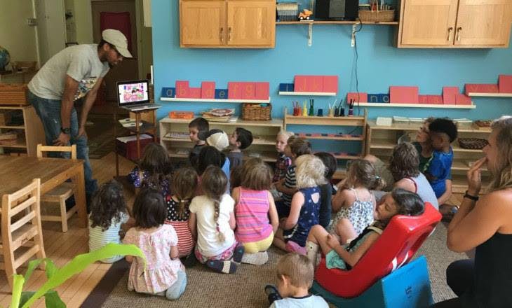 Person showing children something on a laptop in a classroom