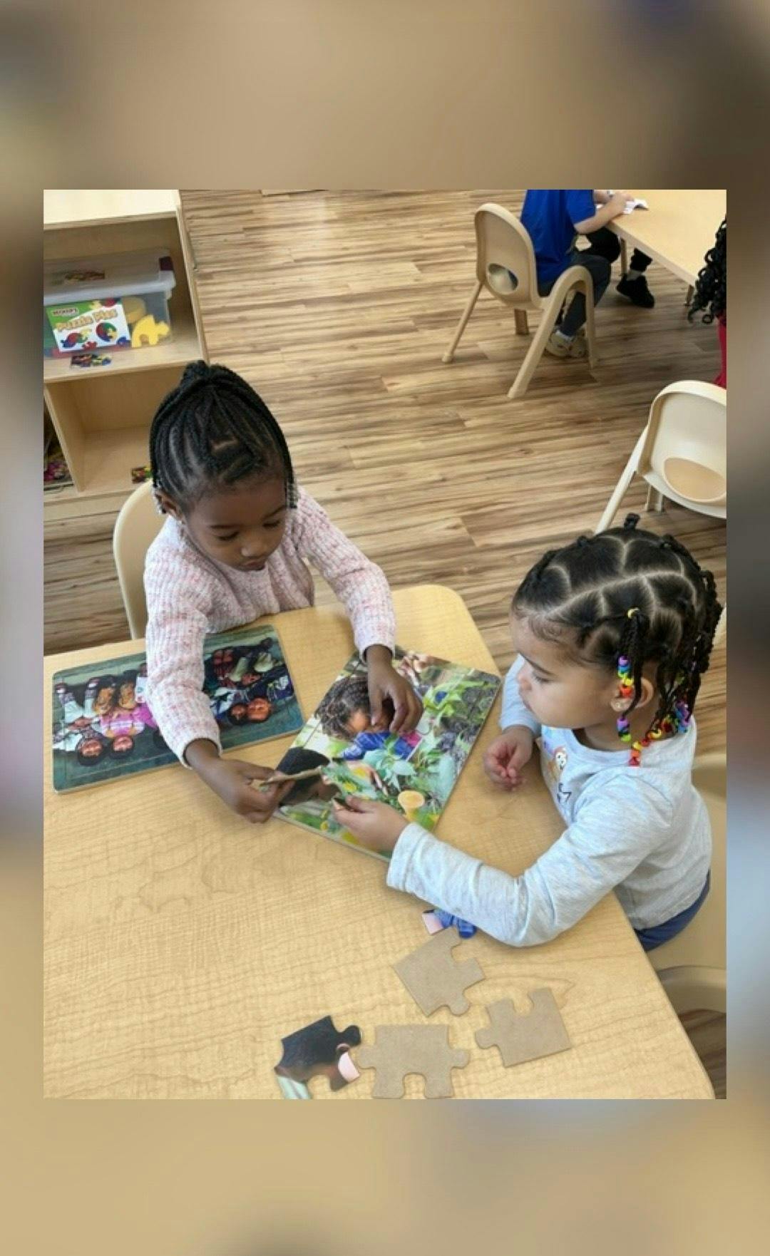 Two children working on a puzzle at a table in a classroom