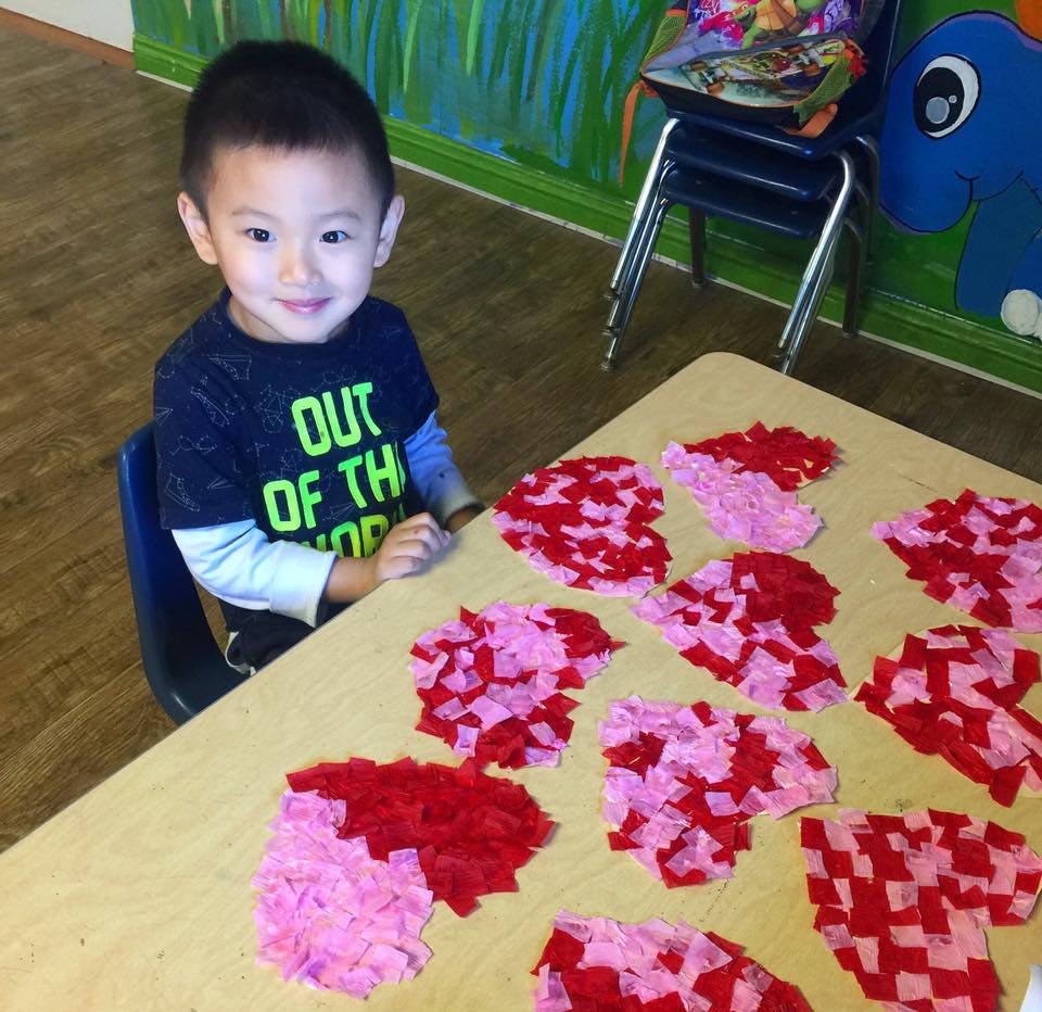 Child sitting at a table with heart-shaped crafts