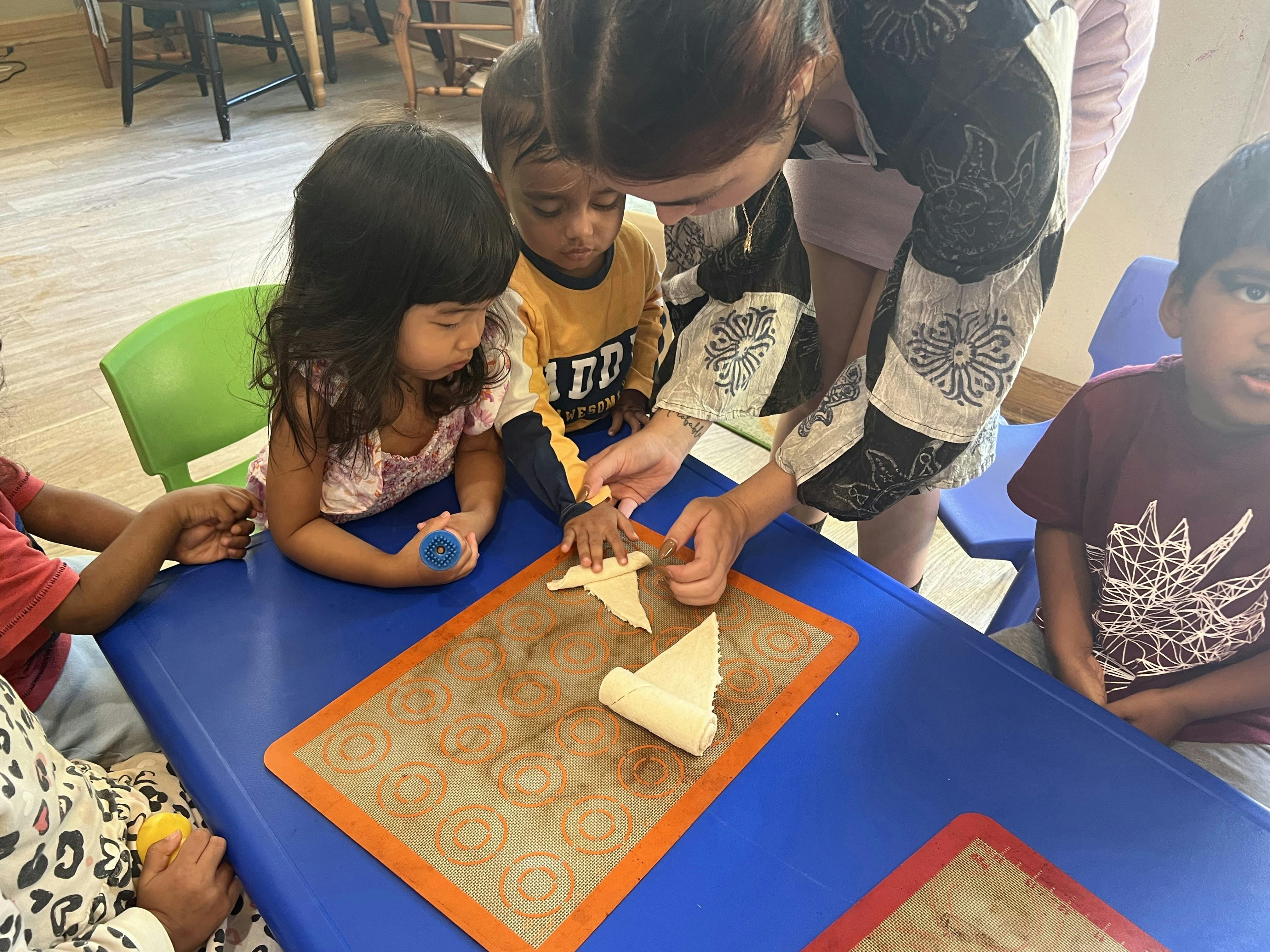Adult helping children roll dough on a silicone mat