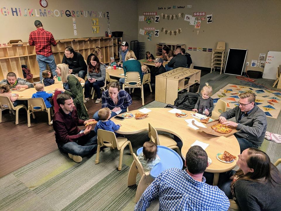 People and children eating pizza in a classroom