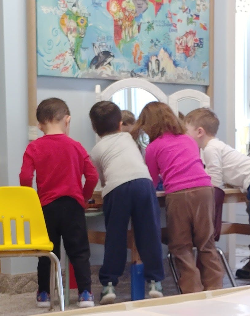 Several children gathered around a mirror in a classroom