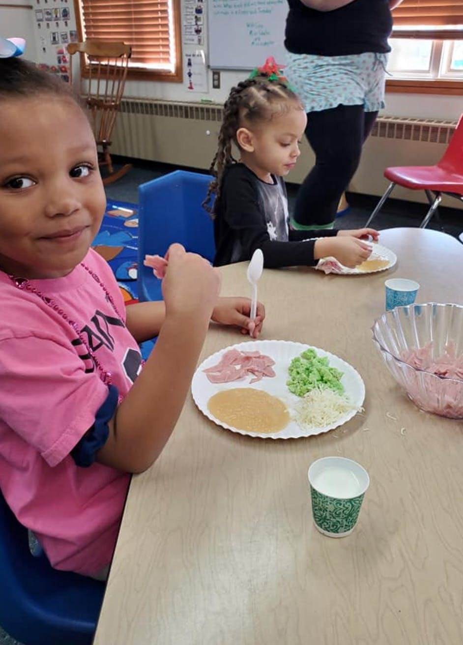 Child at a table with a plate of food items and a spoon
