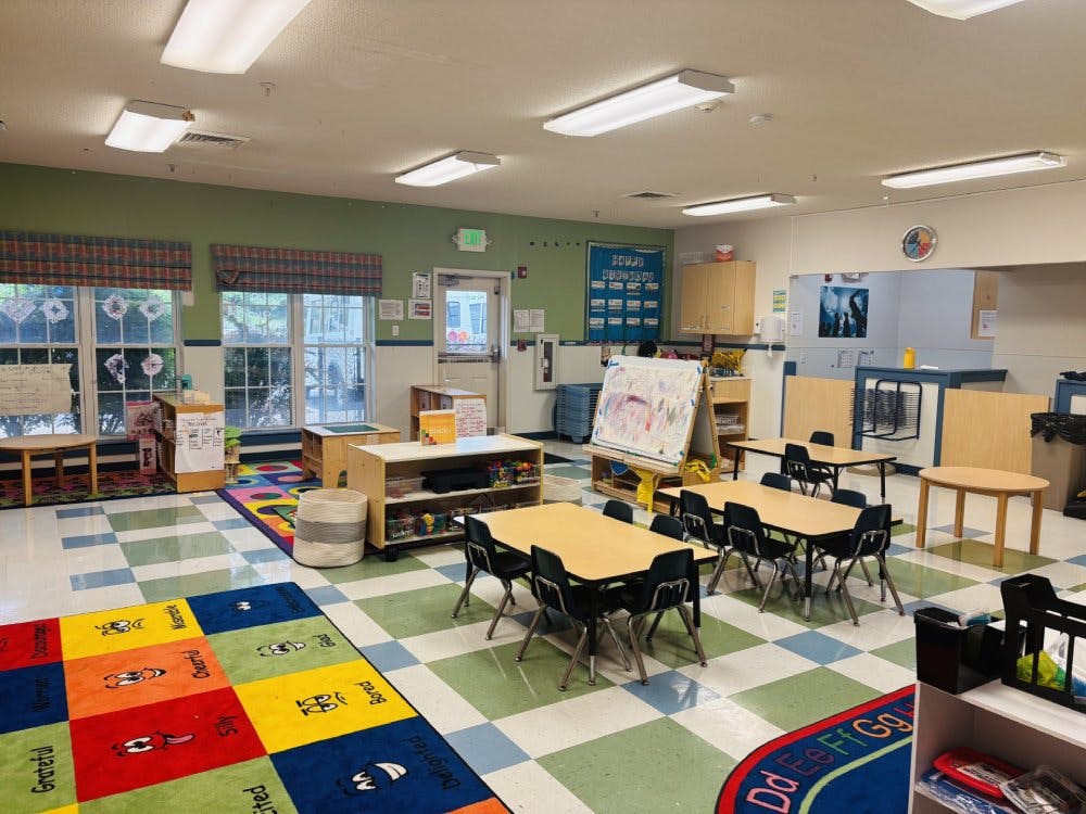 Empty colorful preschool classroom with small tables, chairs, and play areas