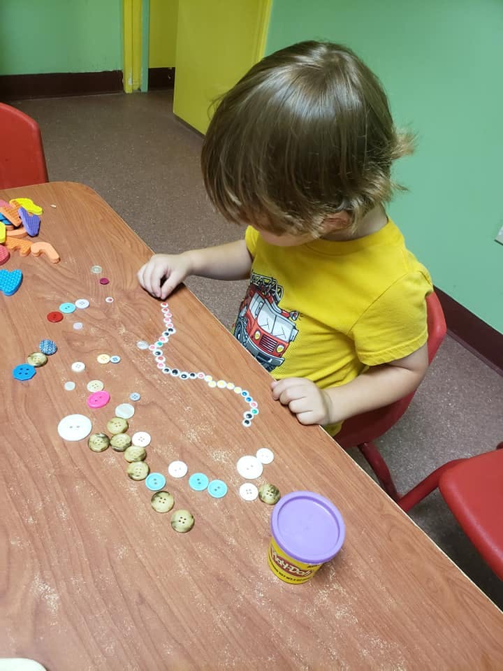Child playing with buttons and a container on a table