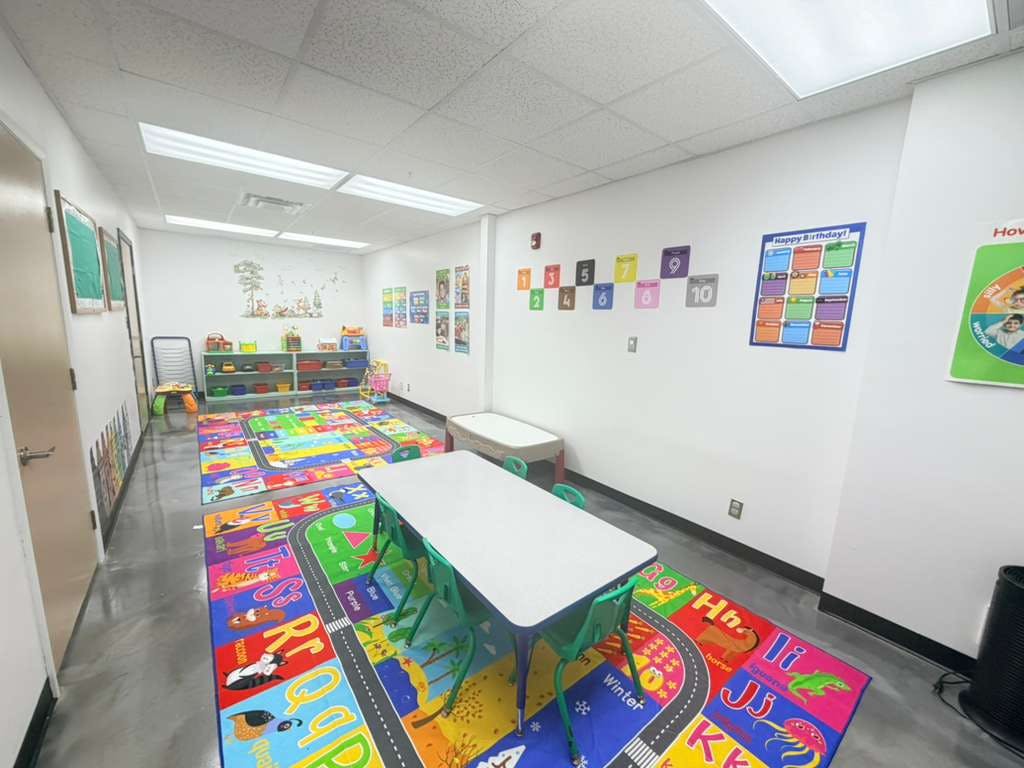 Classroom with colorful rug, small tables and chairs, shelves, and wall decorations