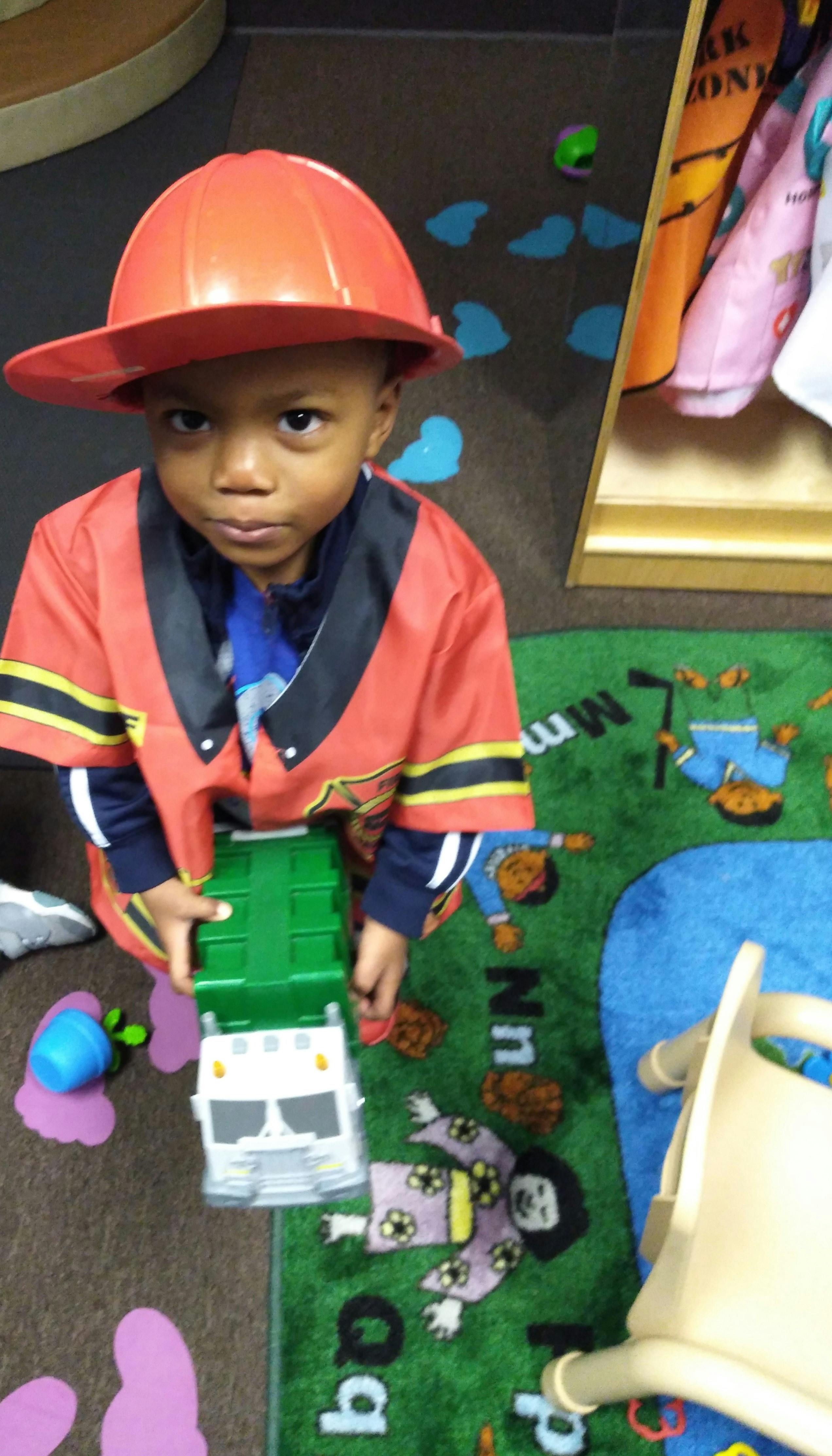 Child in a firefighter costume holding a toy truck