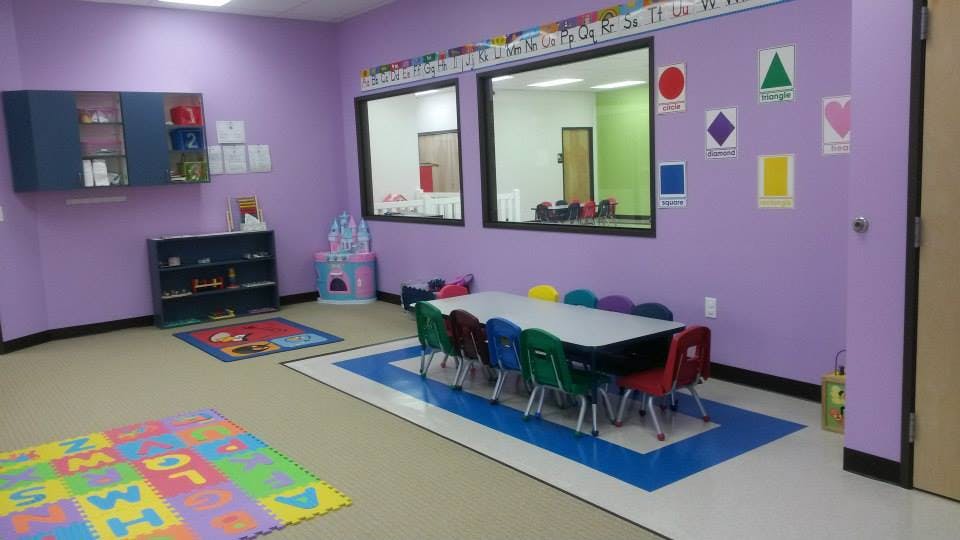 Classroom with purple walls, small table and chairs, and play mats