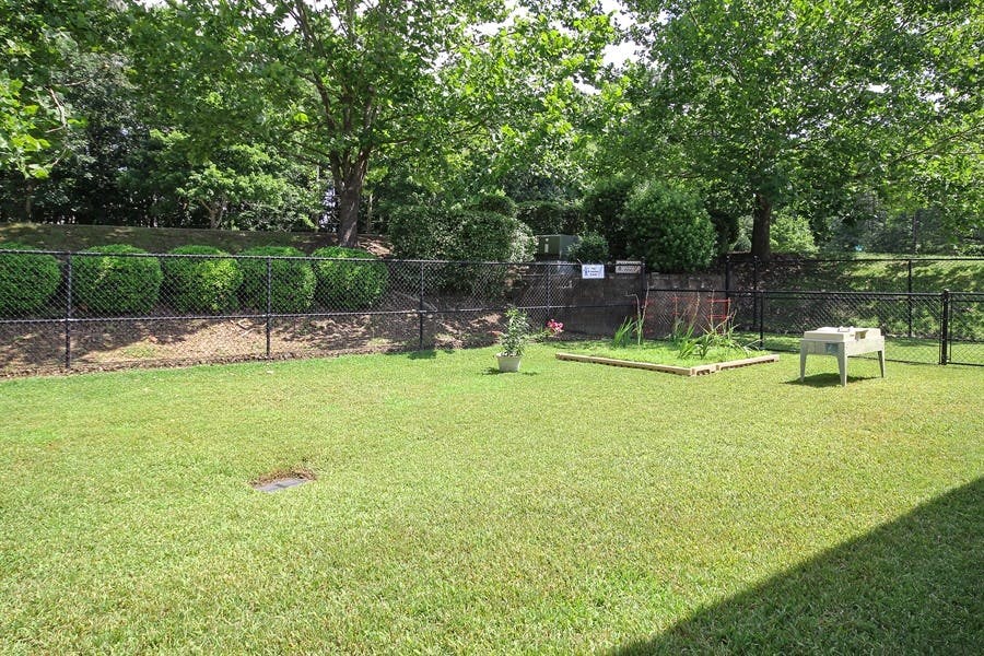Grassy backyard with a fence, trees, and a small garden bed