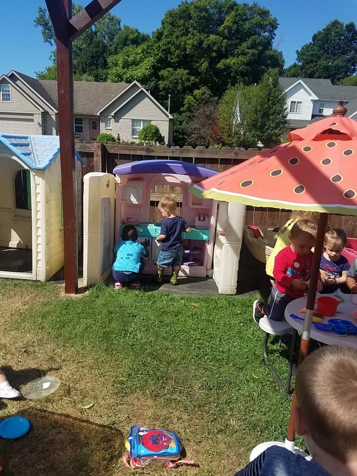 Children playing in a backyard with playhouses and a watermelon umbrella