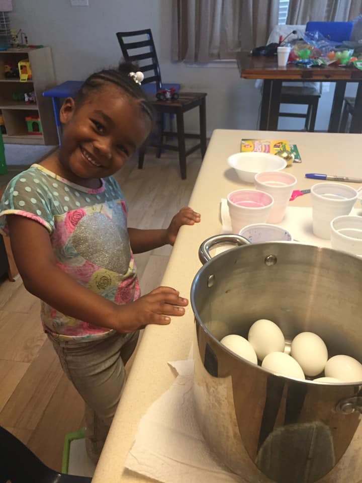 Child standing next to a pot of eggs and cups on a counter