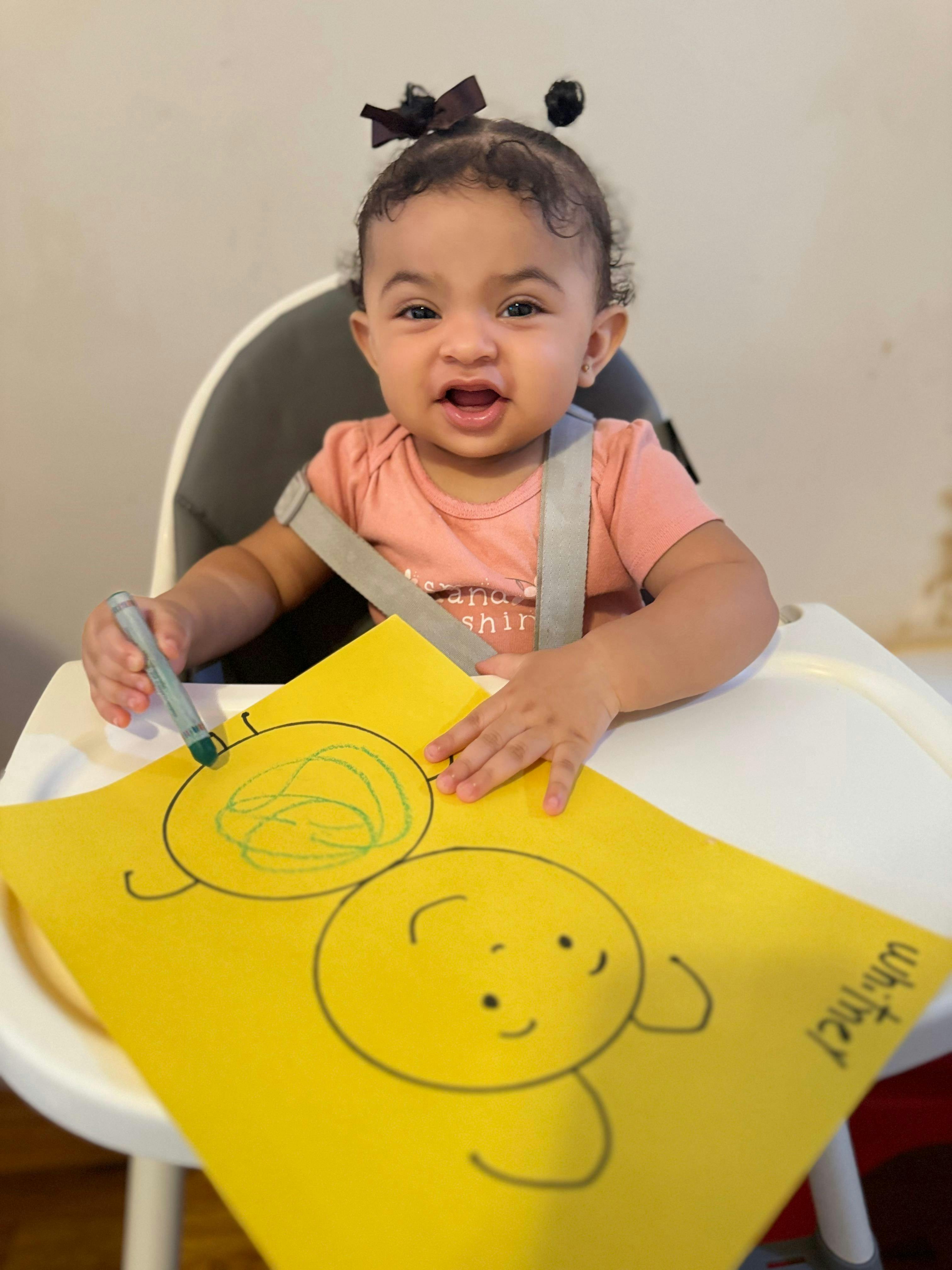 Child drawing on yellow paper in a high chair