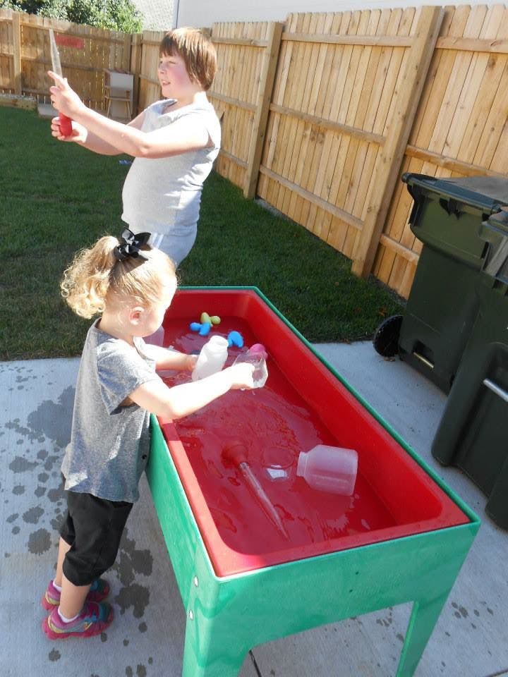Two children playing with water in a red and green water table