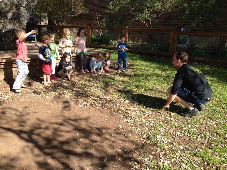 Person crouching on grass facing a group of children