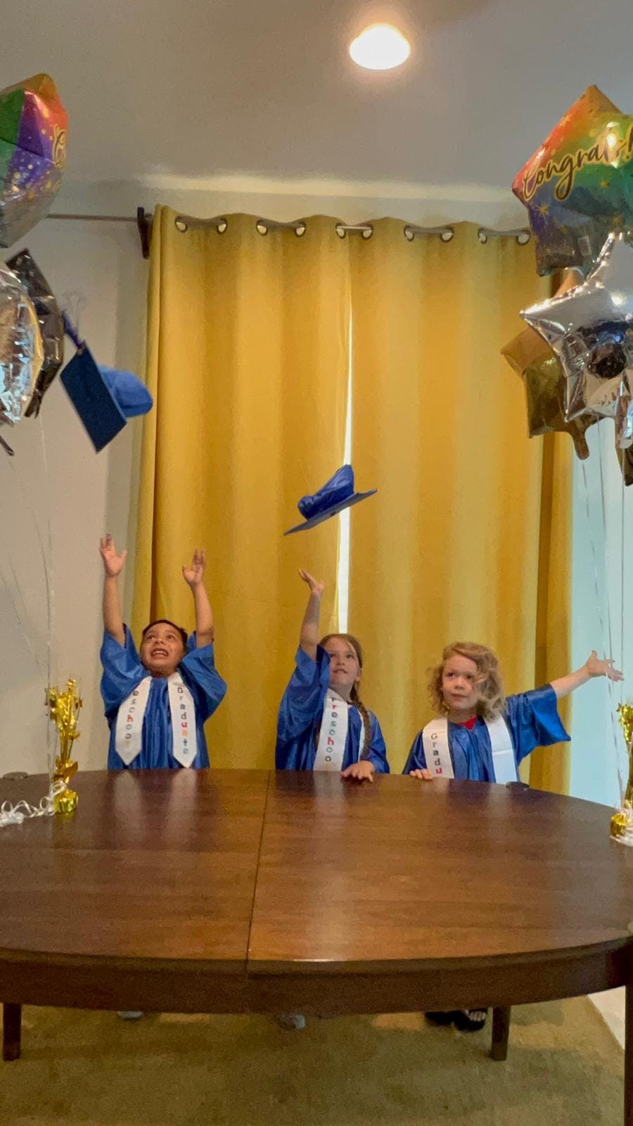 Three children in graduation gowns throwing caps in the air