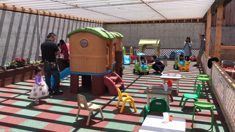 People and children on a playground with play structures and small chairs