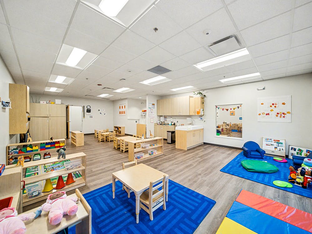 Empty classroom with small tables and chairs, play mats, and toys