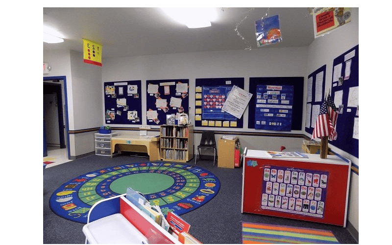 An empty classroom with a round rug and bulletin boards on the walls