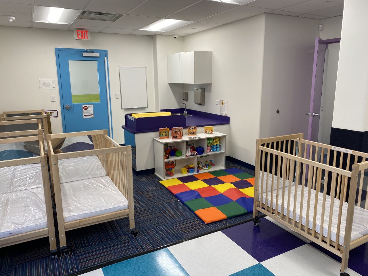 Nursery room with cribs, changing station, and colorful play mat