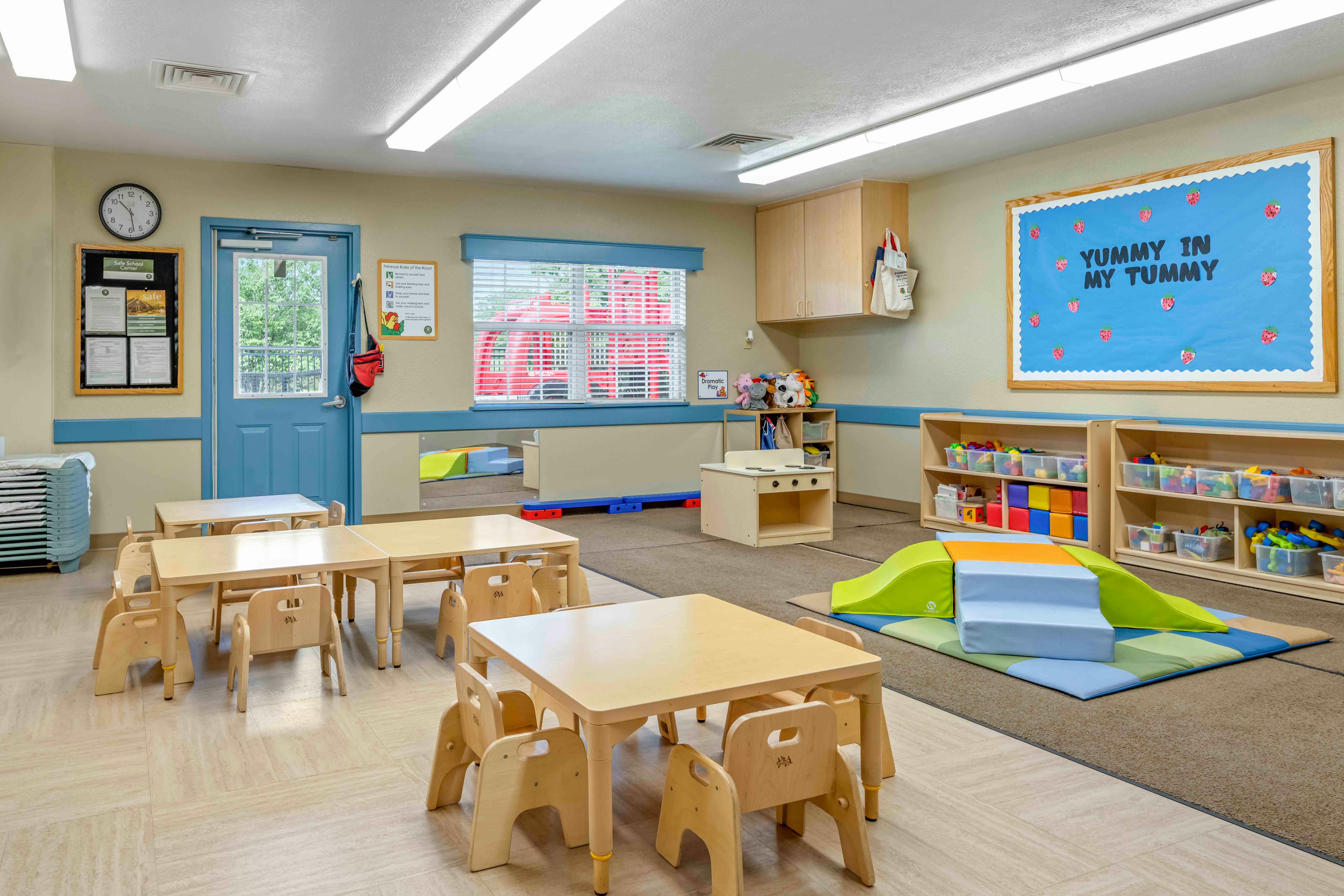 Classroom with child-sized tables and chairs, play area with soft blocks and toys