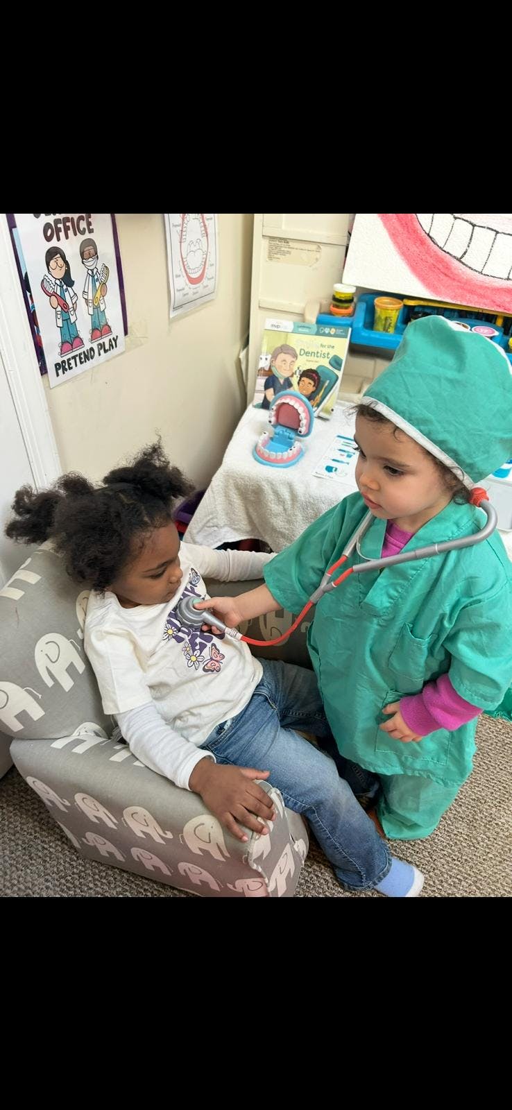Child wearing a green scrubs costume using a toy stethoscope on another child