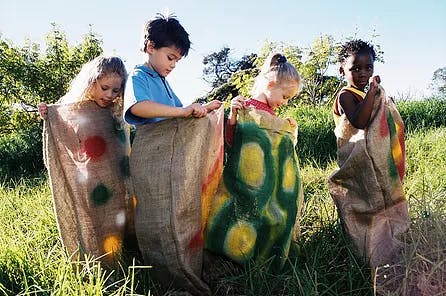 Four children in burlap sacks in a grassy field