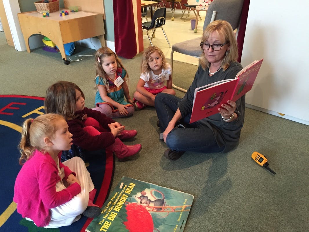 Adult reading a book to four children in a classroom