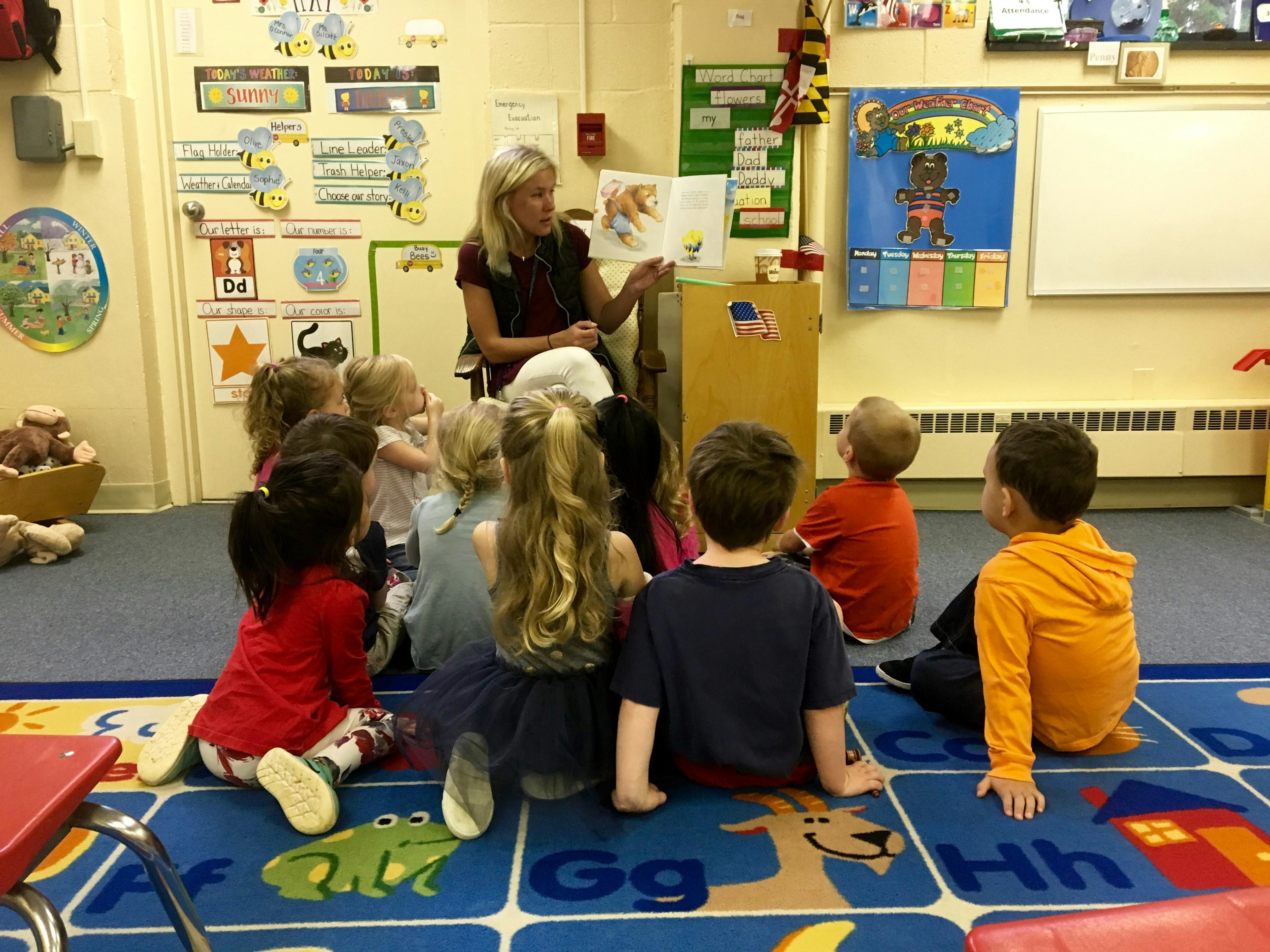 Person reading a book to a group of children in a classroom