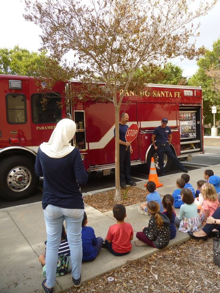 People and children sitting on a sidewalk in front of a fire truck