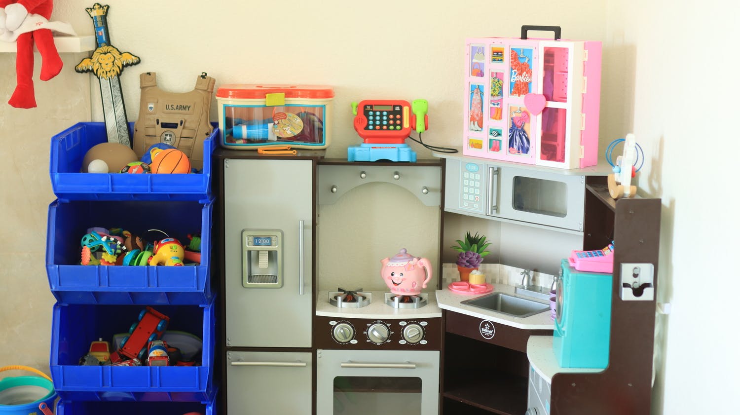 A toy kitchen set with various play accessories and a blue storage bin unit