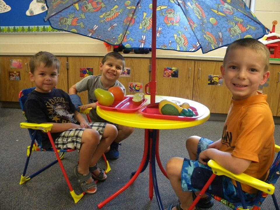 Three children sitting at a small table with an umbrella