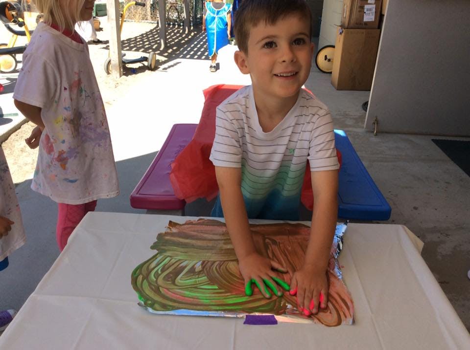 Child finger painting with green and pink paint