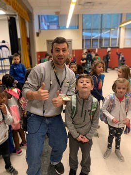 Adult and child giving thumbs up in a room with other children
