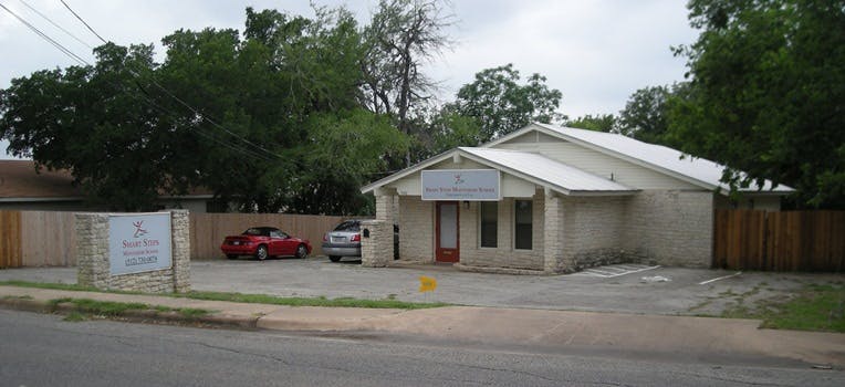Small building with a sign above the entrance and a parking lot with cars