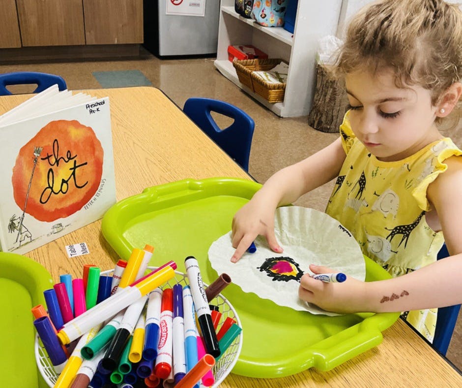 Child coloring a paper plate with markers at a table