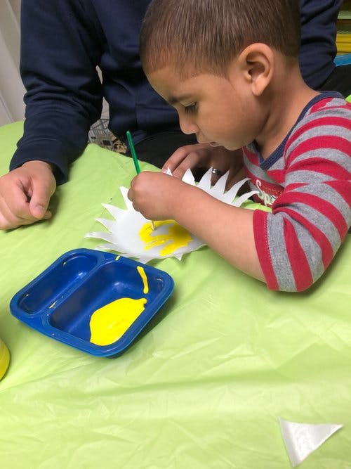 Child painting a paper craft yellow with yellow paint