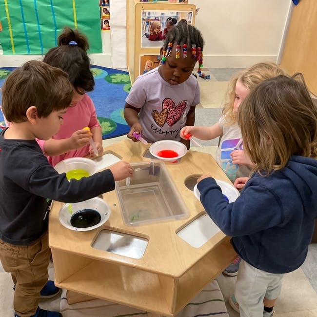 Children playing at a sensory table with colorful liquids